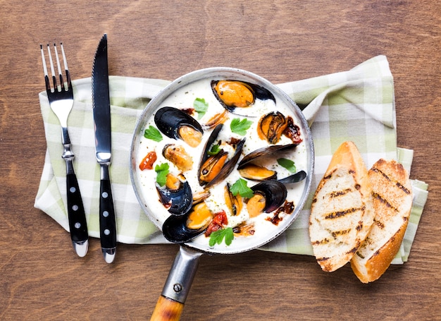 Mejillones planos en salsa blanca con cubiertos sobre mantel