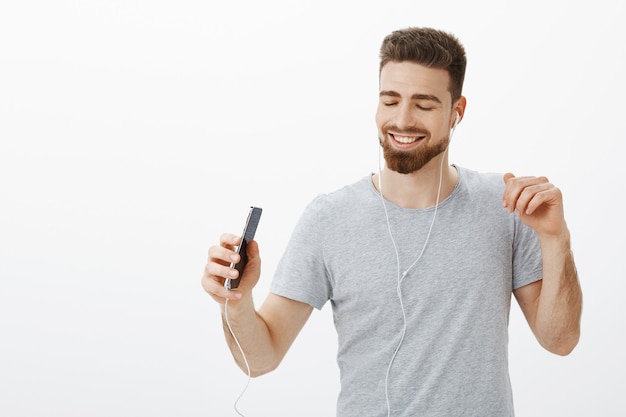 La mejor aplicación de música de todos los tiempos. Alegre, carismático, despreocupado, guapo, con barba y cejas enfermas, cerrando los ojos de deleite y alegría, sonriendo ampliamente sosteniendo teléfonos inteligentes escuchando canciones en auriculares, bailando