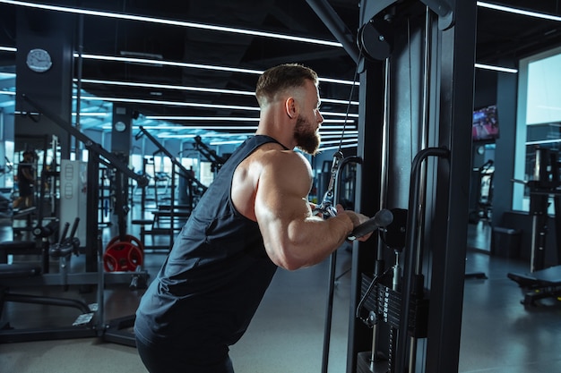 Mejor elección. Joven atleta caucásico muscular entrenando en el gimnasio, haciendo ejercicios de fuerza, practicando, trabajando en la parte superior de su cuerpo con pesas y barra. Fitness, bienestar, concepto de estilo de vida saludable.