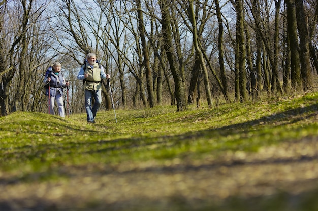 El mejor lugar del mundo. Familia de ancianos pareja de hombre y mujer en traje de turista caminando en el césped cerca de árboles en un día soleado