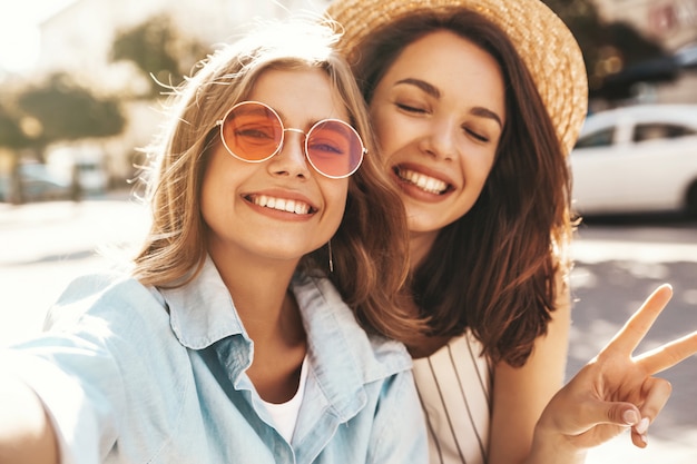 Mejores amigos con atuendo elegante y tomando selfie en la calle