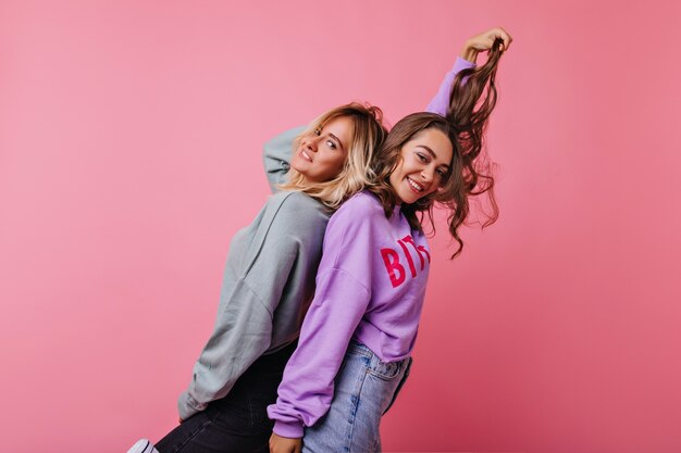 Mejores amigos felices divirtiéndose juntos. Chica morena relajada jugando con su cabello oscuro mientras se relaja con su hermana.