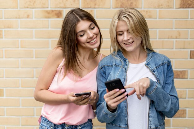 Mejores amigos mirando en sus teléfonos móviles afuera