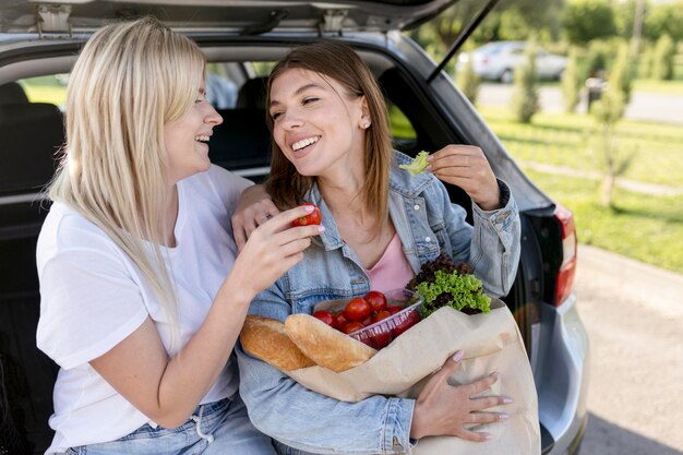 Mejores amigos sentados en el baúl de un automóvil mientras sostienen una bolsa de compras