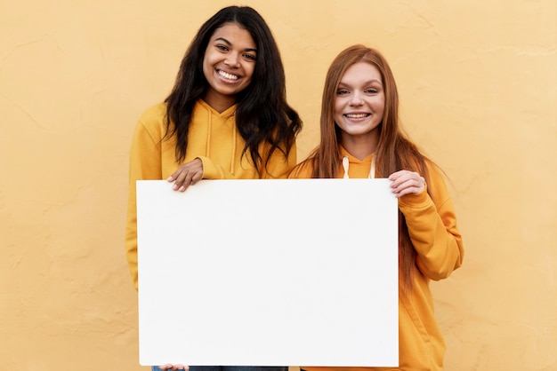 Foto gratuita mejores amigos sosteniendo una tarjeta en blanco