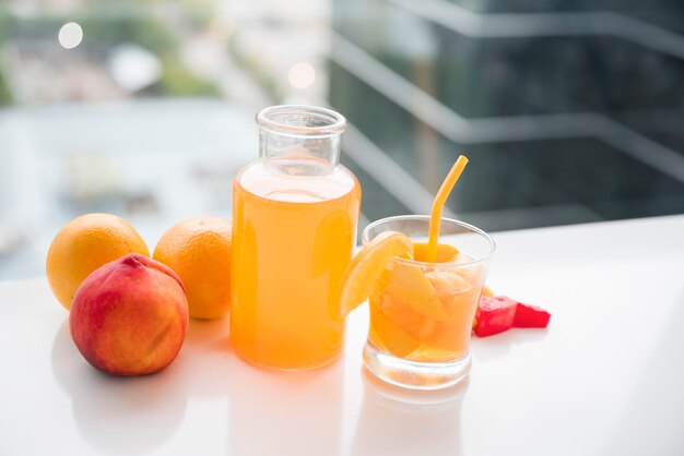 Melocotón; Botella de naranja y jugo y vaso de jugo en escritorio blanco