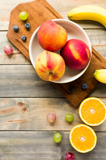 Melocotón; manzanas; uvas; arándanos; Plátano y naranjas a la mitad en el escritorio de madera