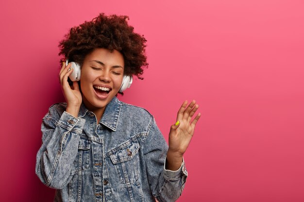 Meloman mujer étnica feliz levanta la palma, escucha la pista de audio en auriculares modernos