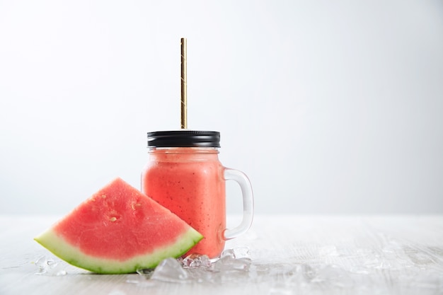 Melón de agua cerca de batido fresco aislado en mesa de madera entre hielo derretido en tarro transparente rústico