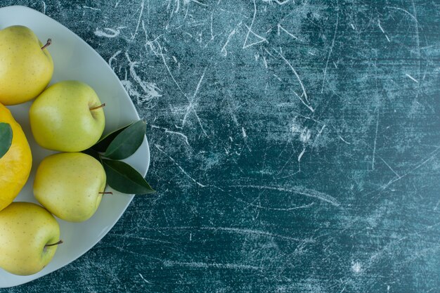 Membrillo y manzanas en un plato, sobre la mesa de mármol.