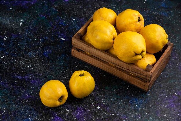 Membrillos enteros maduros en caja de madera sobre mesa oscura.