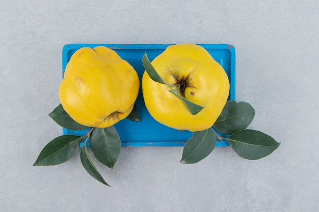 Membrillos enteros maduros con hojas sobre placa azul