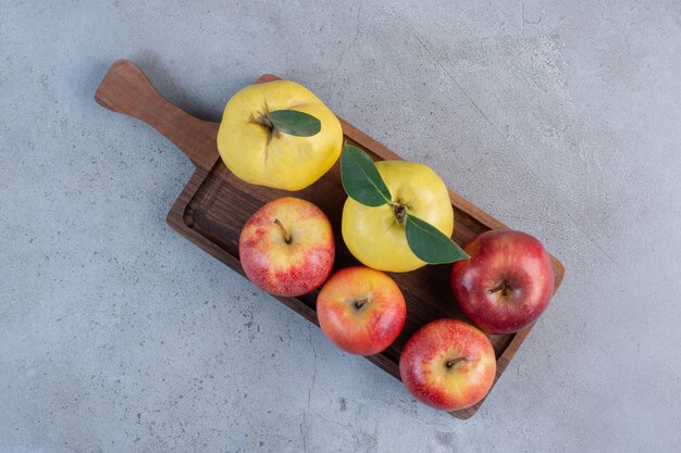 Membrillos y manzanas agrupados sobre una tabla de madera sobre fondo de mármol.