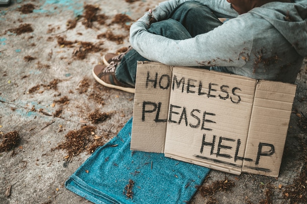 Mendigos sentados en la calle con mensajes de personas sin hogar por favor ayuda.