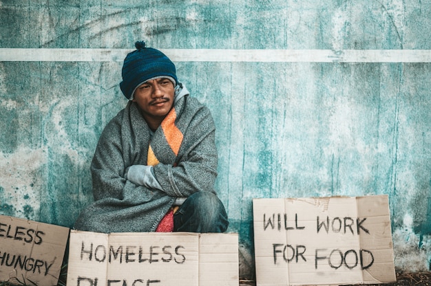 Los mendigos se sentaron al lado de la calle con un mensaje para personas sin hogar. Por favor ayuda y trabaja con la comida.