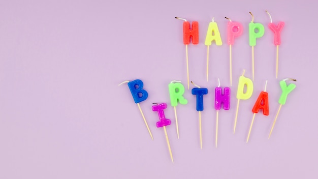 Mensaje de feliz cumpleaños con velas de colores sobre fondo purle