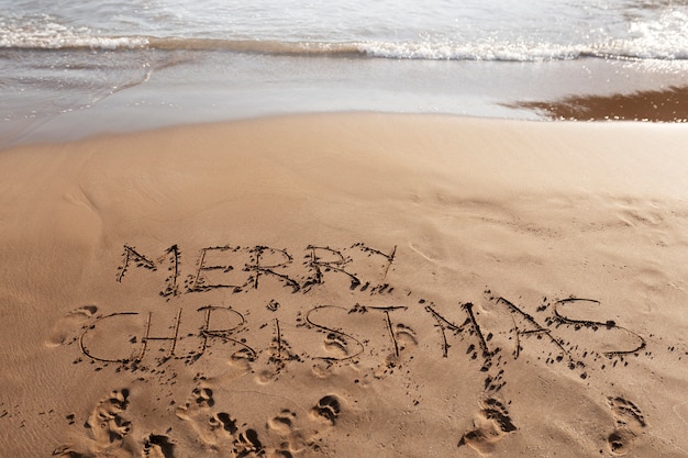 Foto gratuita mensaje de feliz navidad de alto ángulo en la arena