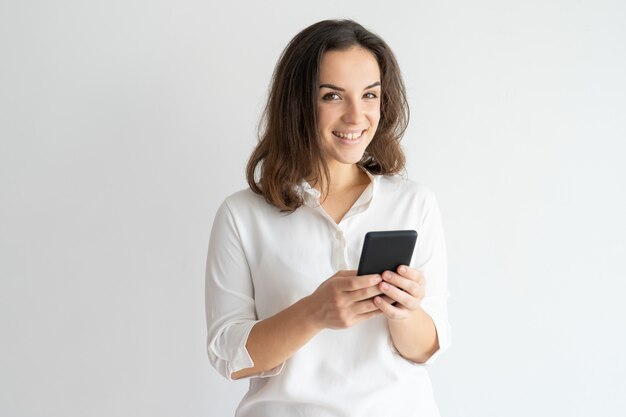 Mensaje sonriente alegre de la muchacha que manda un SMS o que disfruta de la nueva aplicación.