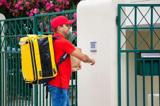 Mensajero de alimentos en uniforme con mochila isotérmica y timbre de timbre de paquete de papel. Concepto de servicio de envío o entrega