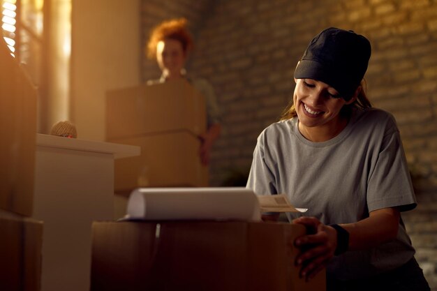 Mensajero femenino feliz preparando el paquete para la entrega mientras trabaja en la oficina