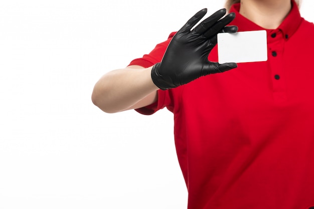 Un mensajero femenino joven de la vista frontal en la camisa roja guantes de cuero negros que sostienen la tarjeta blanca en el servicio uniforme del fondo blanco que entrega