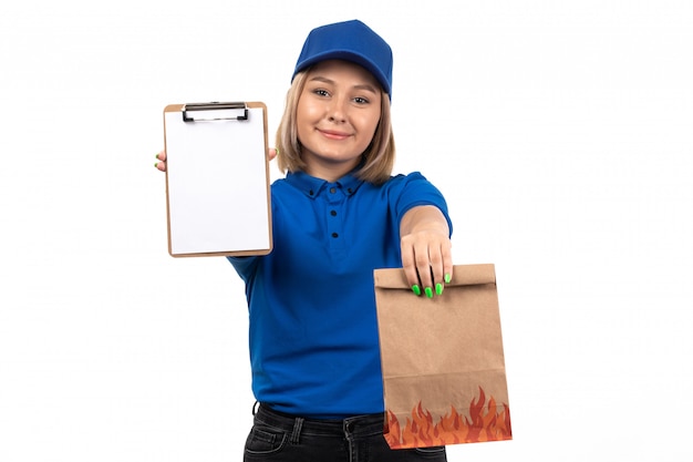 Un mensajero femenino joven de vista frontal en uniforme azul que sostiene el paquete de entrega de alimentos y el bloc de notas para firmas