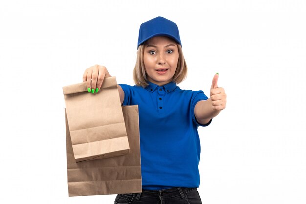 Un mensajero femenino joven de la vista frontal en uniforme azul que sostiene los paquetes de entrega de alimentos