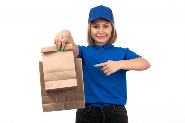 Un mensajero femenino joven de la vista frontal en uniforme azul que sostiene los paquetes de entrega de alimentos