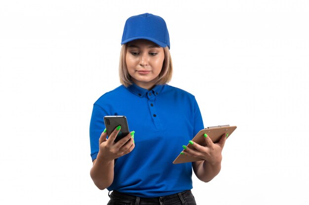 Un mensajero femenino joven de la vista frontal en uniforme azul que sostiene el teléfono y el bloc de notas