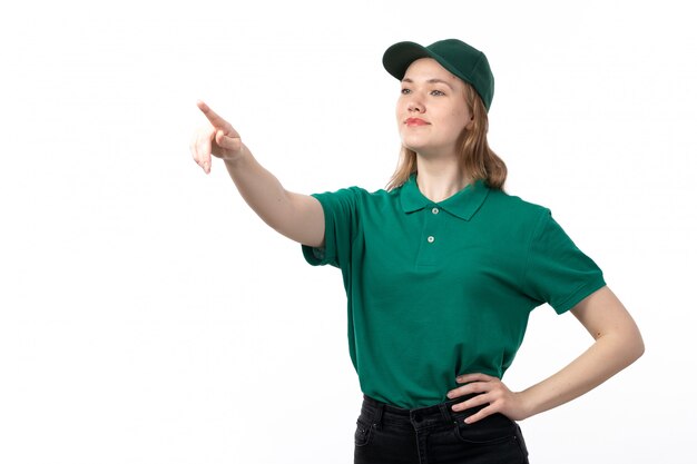 Un mensajero femenino joven de la vista frontal en uniforme verde que sonríe apuntando en la distancia