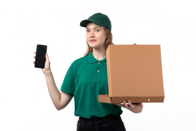 Un mensajero femenino joven de la vista frontal en uniforme verde que sostiene el teléfono inteligente y una caja vacía sonriendo