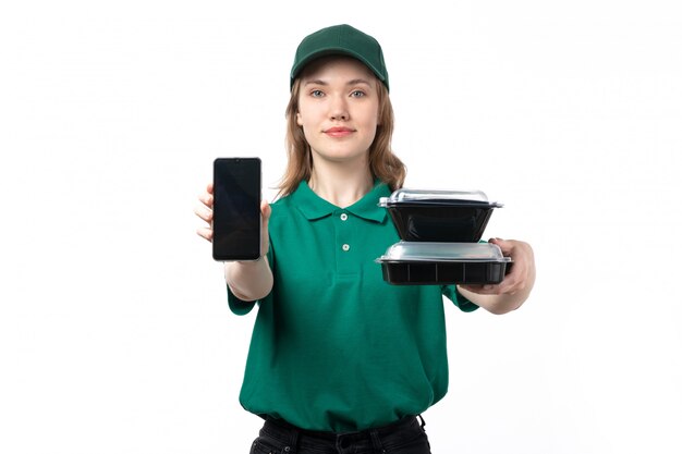 Un mensajero femenino joven de la vista frontal en uniforme verde que sostiene el teléfono inteligente y cuencos con comida