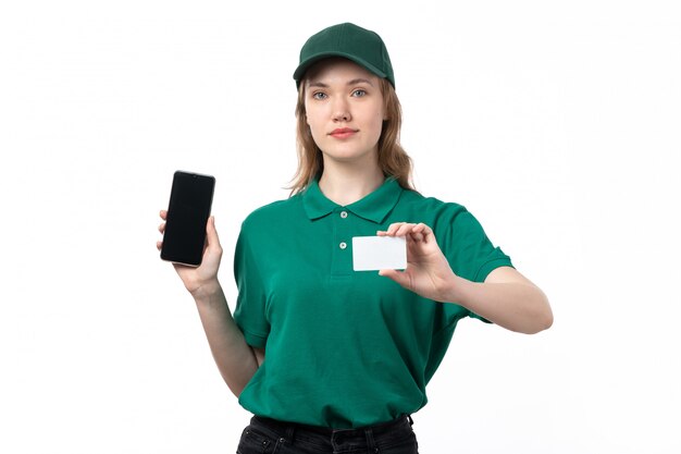 Un mensajero femenino joven de la vista frontal en uniforme verde que sostiene el teléfono inteligente y la tarjeta blanca