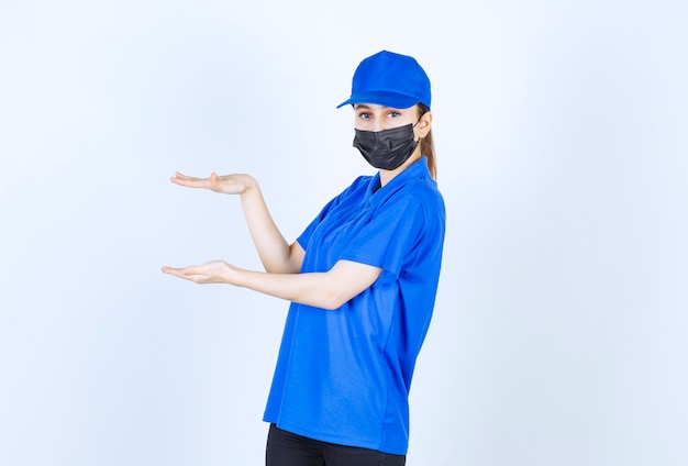 Foto gratuita mensajero femenino en máscara y uniforme azul que muestra la altura de un objeto