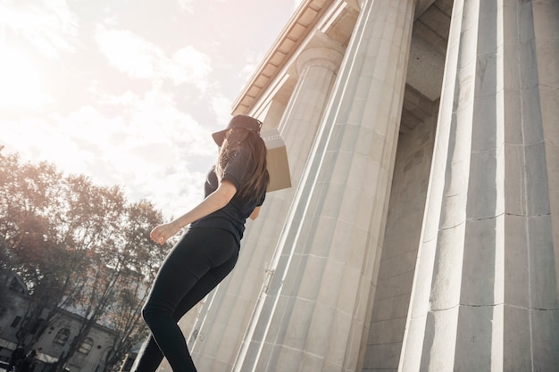Foto gratuita mensajero femenino con parcela caminando cerca de la columna de hormigón