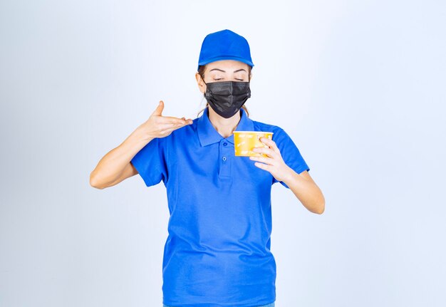 Mensajero femenino del restaurante en uniforme azul y mascarilla sosteniendo una comida para llevar.