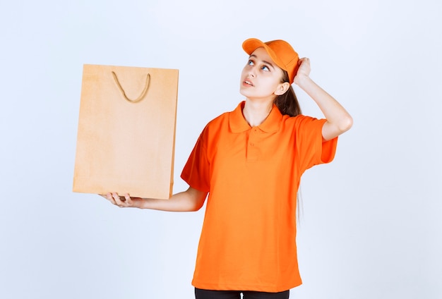 Mensajero femenino en uniforme amarillo entregando una bolsa de compras y parece pensativo