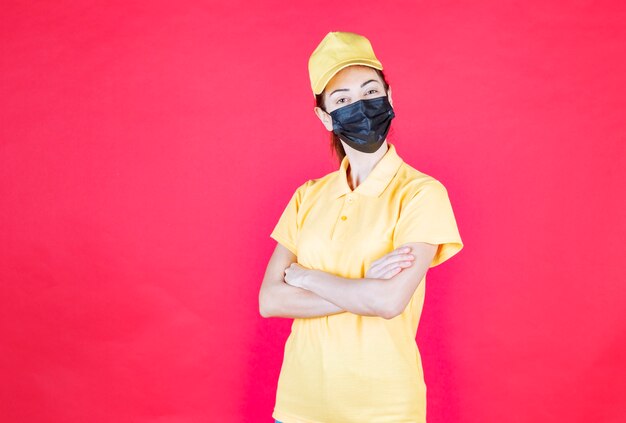 Mensajero femenino en uniforme amarillo y máscara negra cruzando los brazos y parece seguro