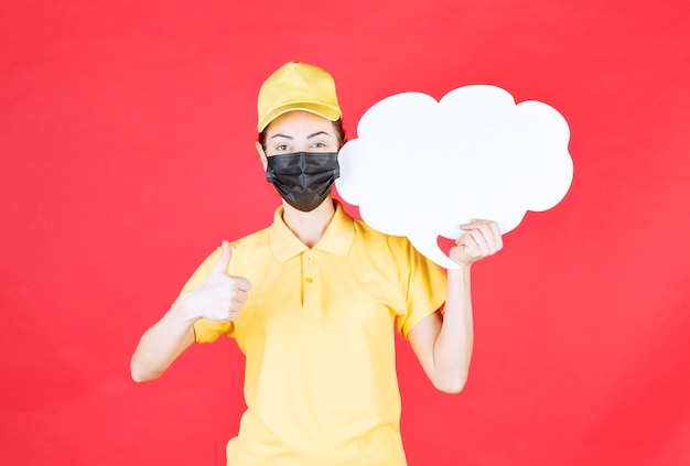 Mensajero femenino en uniforme amarillo y máscara negra sosteniendo un tablero de información en forma de nube y mostrando un signo de disfrute