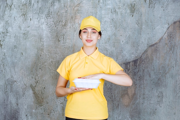 Mensajero femenino en uniforme amarillo que entrega una caja de comida para llevar blanca.