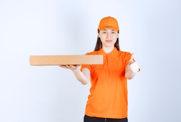 Mensajero femenino en uniforme amarillo sosteniendo una caja de cartón para llevar y mostrando el signo de la mano de disfrute.