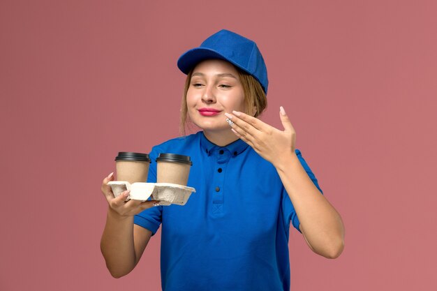 Mensajero femenino en uniforme azul posando y sosteniendo tazas de café con olor a rosa, trabajo de entrega uniforme de servicio