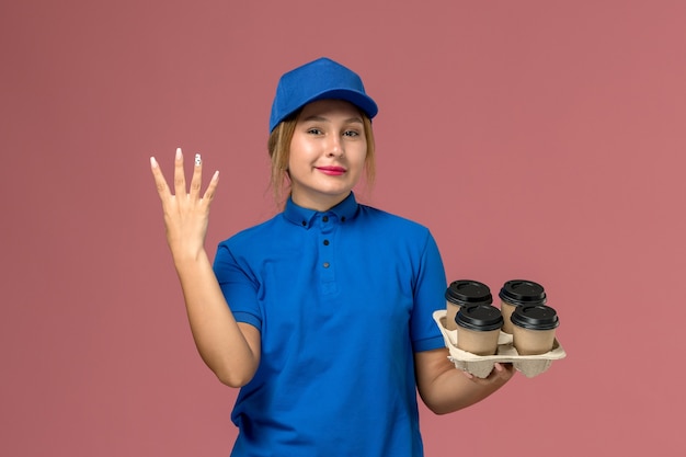 Mensajero femenino en uniforme azul sosteniendo tazas de café de entrega marrón mostrando el número cuatro en rosa, trabajador de trabajo de entrega uniforme de servicio