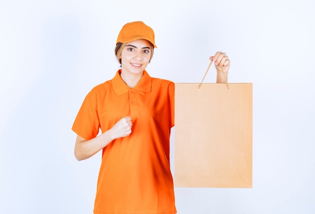 Mensajero femenino en uniforme naranja entregando una bolsa de cartón y mostrando el signo de disfrute