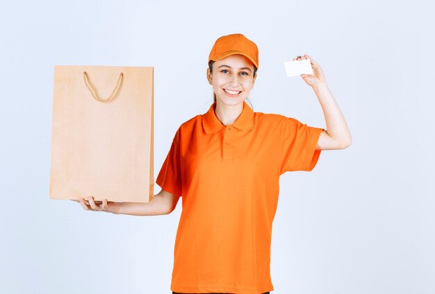 Mensajero femenino en uniforme naranja entregando una bolsa de compras y presentando su tarjeta de visita