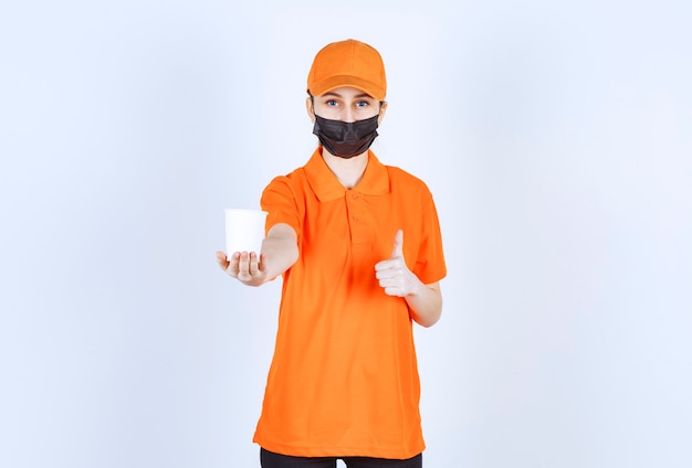 Mensajero femenino en uniforme naranja y máscara negra sosteniendo una bebida para llevar y disfrutando del sabor