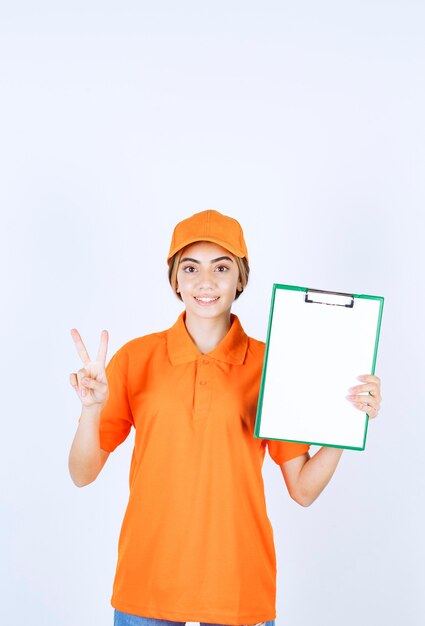 Foto gratuita mensajero femenino en uniforme naranja que muestra una lista de clientes y muestra un signo de satisfacción