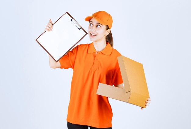 Mensajero femenino en uniforme naranja sosteniendo una caja de cartón abierta y pidiendo una firma