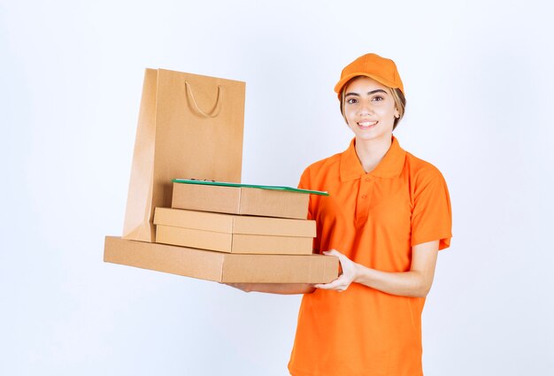 Mensajero femenino en uniforme naranja sosteniendo un stock de paquetes de cartón y bolsas de la compra.