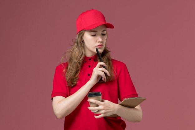Mensajero femenino en uniforme rojo con bolígrafo y taza de café en rosa, trabajador de trabajo de entrega de servicio uniforme